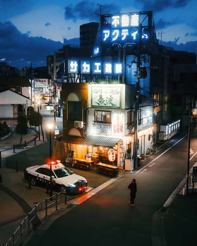 A Japanese street corner at dusk, covered in lit shop signs